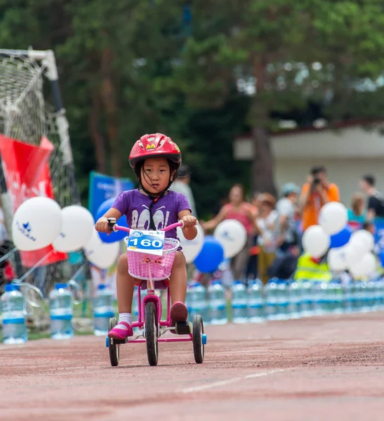 KAZAKHSTAN, ALMATY - 11 de junio de 2017: Concursos de ciclismo infantil Tour de kids. Los niños de 2 a 7 años compiten en el estadio y reciben premios. La chica en bicicleta monta en un estadio deportivo — Foto de Stock