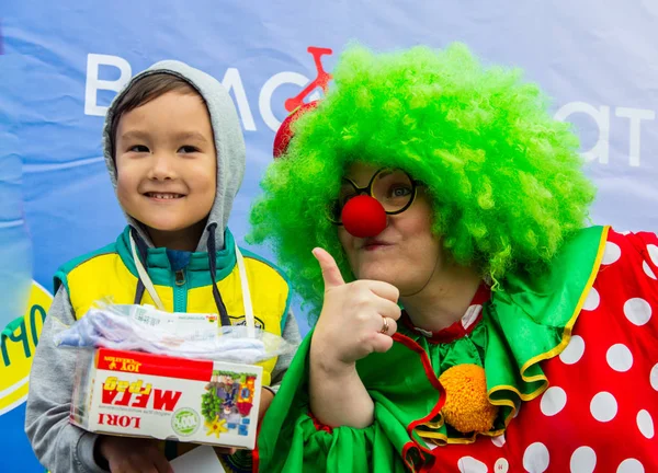KAZAKHSTAN, ALMATY - 11 JUIN 2017 : Compétitions cyclistes pour enfants Tour de kids. Les enfants âgés de 2 à 7 ans concourent dans le stade et reçoivent des prix. Petite fille et clown jouent aux palmiers . — Photo