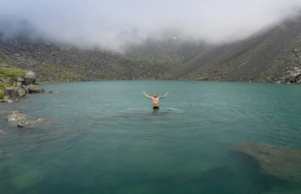 Ein Mann badet bei regnerischem Wetter in einem kalten Bergsee. See der Berggeister, Altai, Russland. — Stockfoto