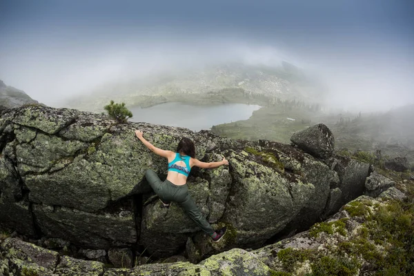 Giovane donna che indossa attrezzature da arrampicata in piedi davanti a una roccia di pietra all'aperto e si prepara a salire, vista posteriore — Foto Stock