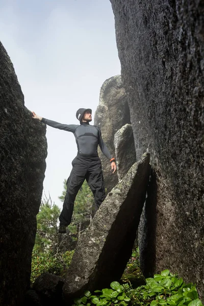 Männlicher Bergsteiger. Bergsteiger klettert auf eine schwarze Felswand am Ufer des Ozeans in Island, am Strand von Kirkjufjara. Mann macht schweren Schritt ohne Seil. — Stockfoto
