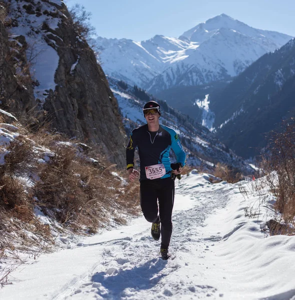 ALMATY, KAZAKHSTAN - 09 APRILE 2017: Concorsi amatoriali - Mezza maratona di montagna, ai piedi di Almaty, sui laghi di Yunat. .Athlete uomo in esecuzione con le montagne in inverno — Foto Stock