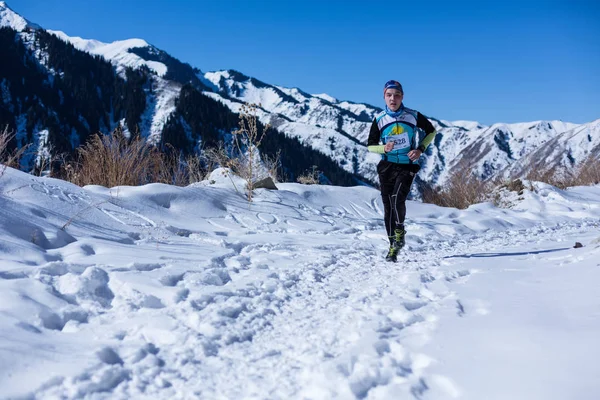 ALMATY, KAZAKHSTAN - 09 APRILE 2017: Concorsi amatoriali - Mezza maratona di montagna, ai piedi di Almaty, sui laghi di Yunat. .Athlete uomo in esecuzione con le montagne in inverno — Foto Stock