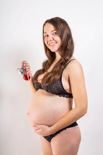 Hermosa chica embarazada sobre un fondo blanco sostiene juguetes de Navidad en sus manos . — Foto de Stock