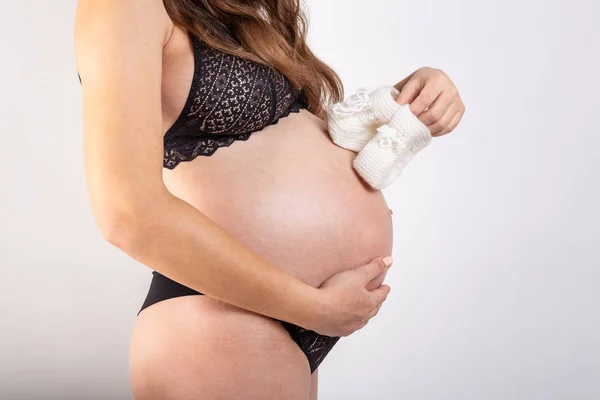 Donna felice incinta che tiene le scarpe da bambino blu nelle sue mani. Mamma si aspetta un bambino. La pancia delle donne incinte. Gravidanza — Foto Stock