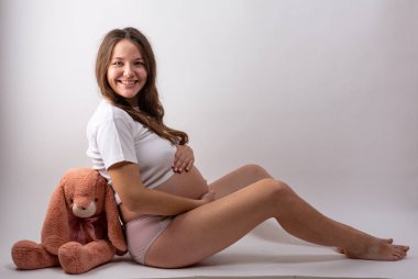 Genç hamile kadın beyaz arka planda oturuyor.