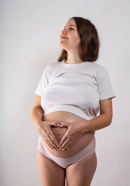 Молодая красивая беременная женщина с длинными здоровыми вьющимися волосами позирует в черном нижнем белье на сером фоне. Активная беременность . — стоковое фото