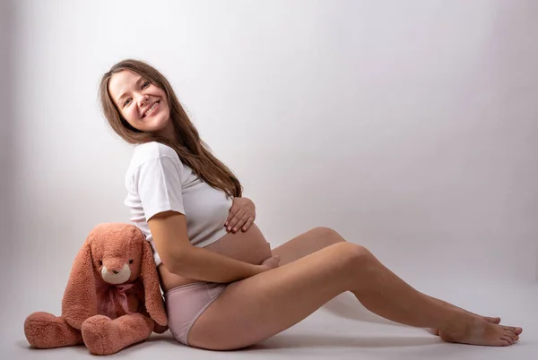 Jeune femme enceinte assise sur fond blanc — Photo