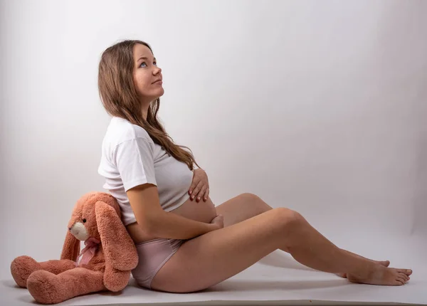 Mladá těhotná žena sedí na bílém pozadí — Stock fotografie