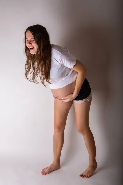 A jovem mulher grávida bonita experimenta emoções fortes em um fundo branco — Fotografia de Stock