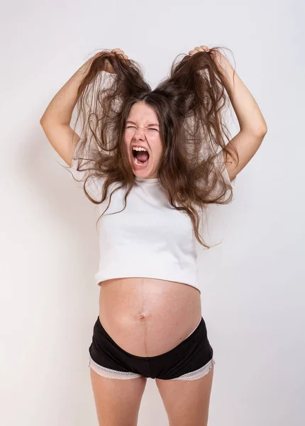 Den unga vackra gravida kvinnan upplever starka känslor på en vit bakgrund — Stockfoto