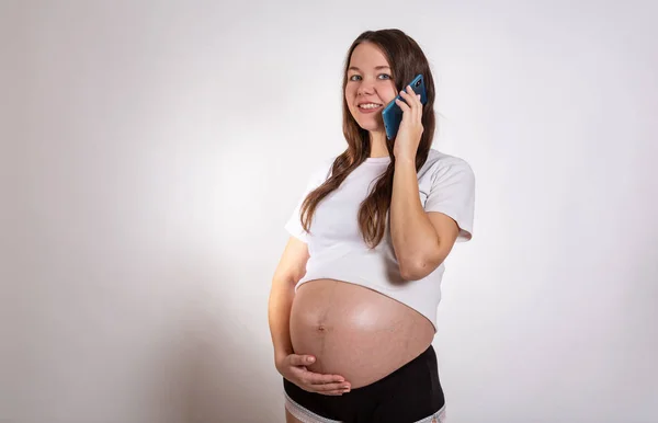 Mulher grávida bonito no telefone enquanto deitado em um fundo branco — Fotografia de Stock