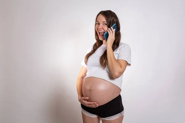 白い背景に横たわっている間、電話でかわいい妊婦 — ストック写真
