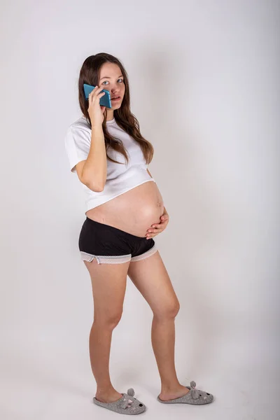 Симпатична вагітна жінка по телефону лежить на білому тлі — стокове фото