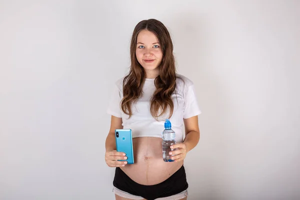 Hermosa mujer embarazada morena beber agua de la botella sobre fondo blanco aislado — Foto de Stock