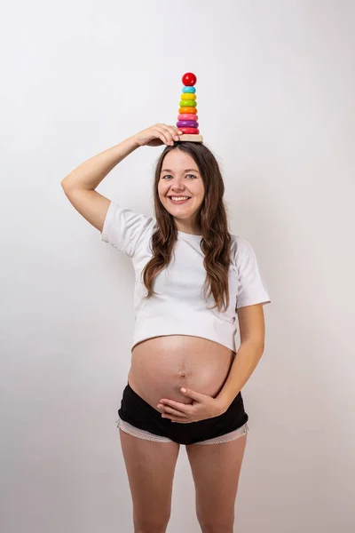 Gravid flicka med en trä regnbåge pyramid för barn. Begreppet förväntad baby. — Stockfoto