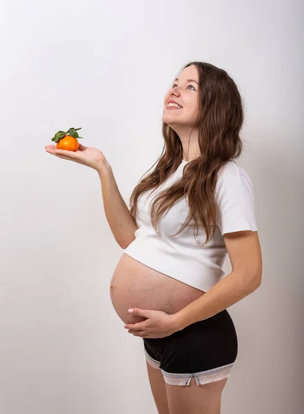 Imagem da mulher grávida tocando sua barriga grande e segurando maçã amarela na mão no fundo branco . — Fotografia de Stock