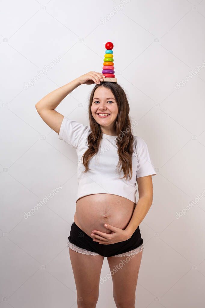 Pregnant girl with a wooden rainbow pyramid for children. Baby expectation concept.