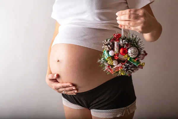 Schwangere lächelt, berührt ihren Bauch, steht über der weißen Wand. Kopierraum. Weihnachten, Neujahrskonzept. — Stockfoto