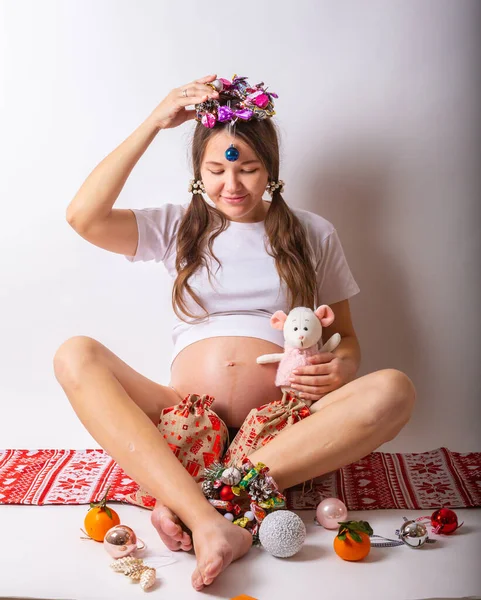 Mujer embarazada sonriendo, tocando su vientre, de pie sobre la pared blanca. Copiar espacio. Navidad, concepto de año nuevo . — Foto de Stock