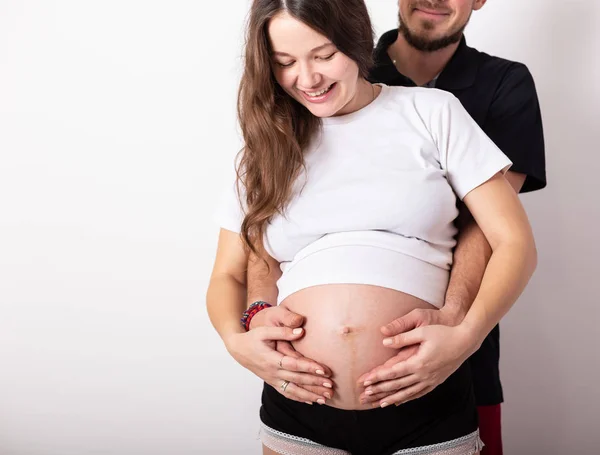 Abgeschnittenes Bild der schönen schwangeren Frau und ihres hübschen Mannes, der den Bauch umarmt — Stockfoto