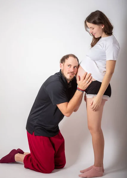 Hombre guapo está escuchando a sus hermosas esposas embarazadas barriga y sonriendo — Foto de Stock