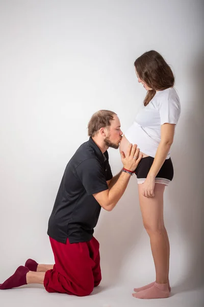 Bel homme écoute sa belle femme enceinte ventre et souriant — Photo