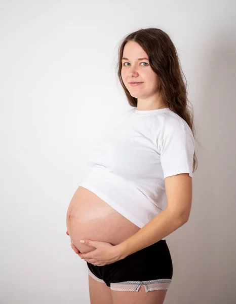 Den unga vackra gravida kvinnan upplever starka känslor på en vit bakgrund — Stockfoto