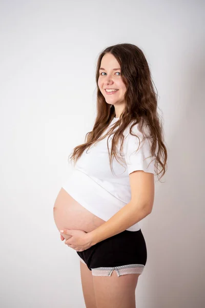 A jovem mulher grávida bonita experimenta emoções fortes em um fundo branco — Fotografia de Stock