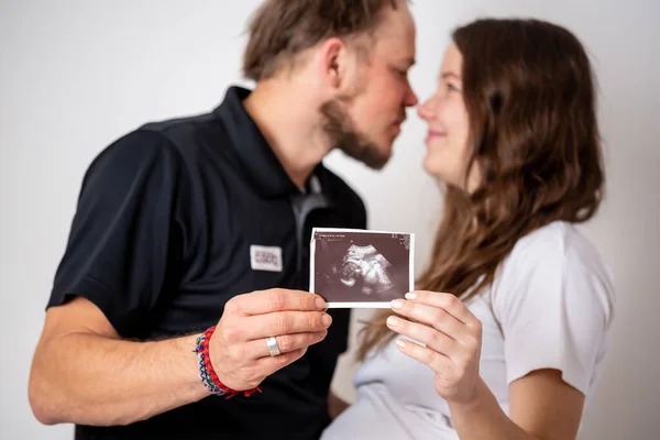 幸福的已婚夫妇正在显示怀孕测试棒和他们未出生的婴儿的超声照片。聚焦两条条纹 — 图库照片