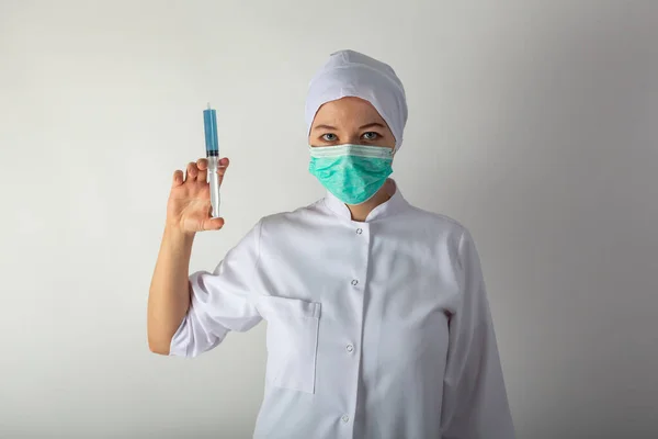 Девушка в медицинском пальто держит большой шприц с голубой жидкостью - коронавирусную вакцину — стоковое фото