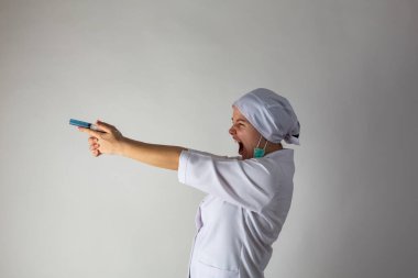 Tıp önlüklü kız silah gibi mavi bir şırınga tutuyor.