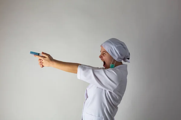 Девушка в медицинском пальто держит большой шприц с голубой жидкостью, как пистолет — стоковое фото