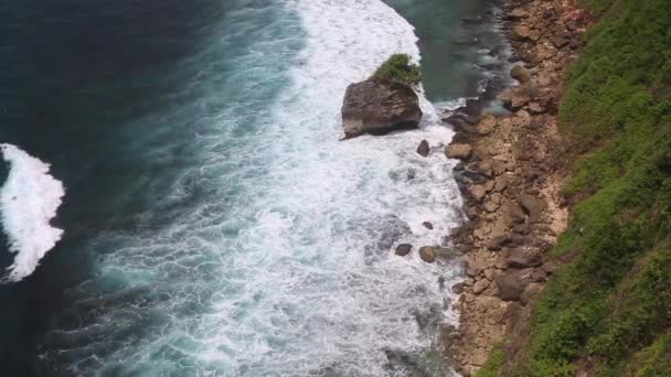 Aerial static view of evening ocean surface, calm waves rolling at rocky shore. Amazing high cliffs above the ocean and Uluwatu temple on the top. Bali, Indonesia — Stock Video