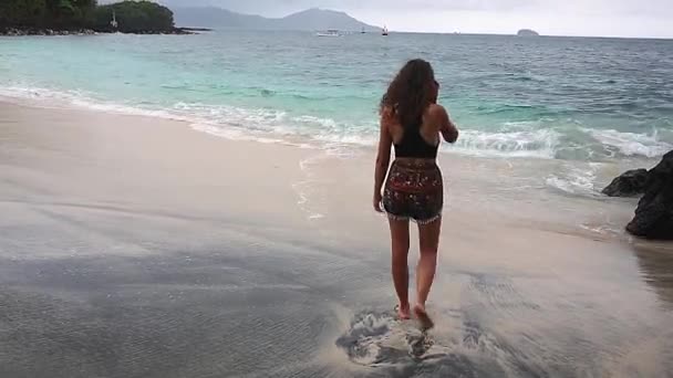 Plajda çıplak ayakla yürüyen, rüzgarda savrulan, açık renk elbiseler giyen bir kadın. — Stok video
