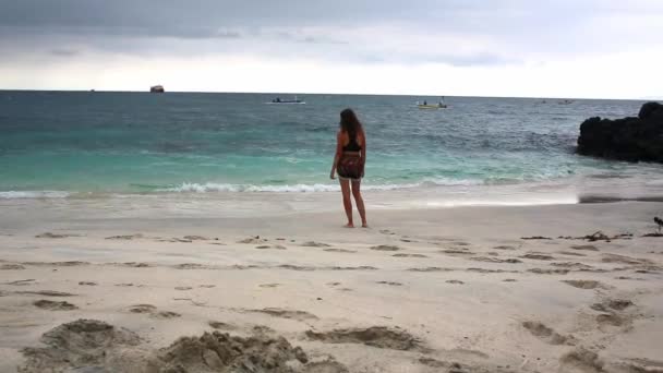 Woman walks along beach barefoot wearing light flowing dress blowing in the wind — Stock Video