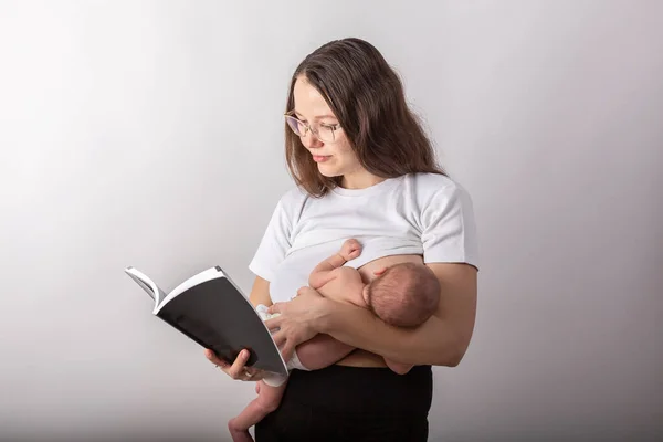 Hermosa madre joven amamantando a un bebé mientras lee un libro negro — Foto de Stock