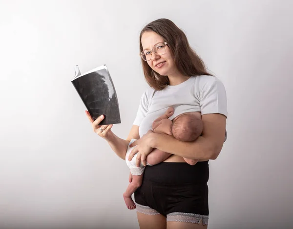Schöne junge Mutter stillt ein Baby, während sie ein Schwarzbuch liest — Stockfoto