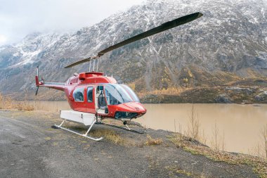 Kırmızı bir helikopter dağ gölünün kenarında boş boş oturuyor.