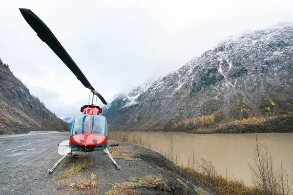 Kırmızı bir helikopter bir dağ gölünün yanında duruyor.