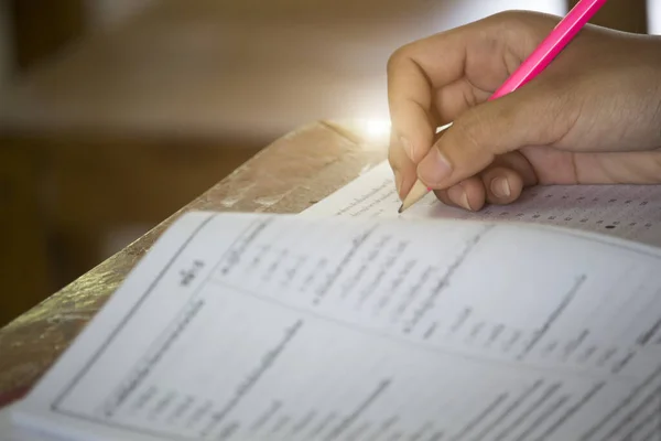 Öğrenciler testi yapıyor, sadece kalem tutan eli görüyor, masanın üzerine yazı yazıyor..