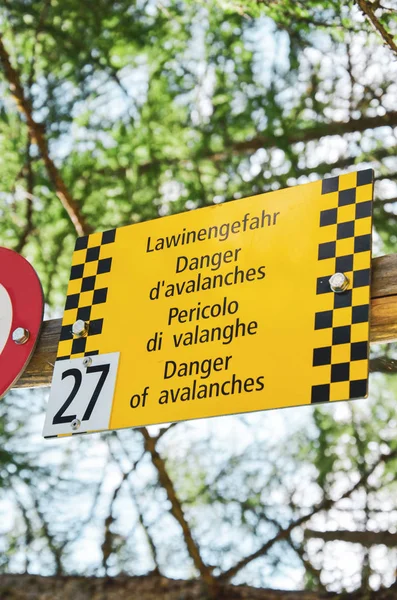 Il cartello turistico giallo avverte delle valanghe in quattro lingue diverse. Avviso in tedesco, francese, italiano e inglese. Segnaletica informativa per i turisti nelle Alpi svizzere — Foto Stock