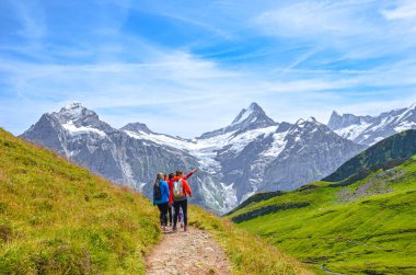 Grindelwald, Switzerland - August 16, 2019: Summer Alpine landscape. Female hikers and Swiss Alps in the background. Photographed on the trail from Grindelwald to Bachalpsee clipart