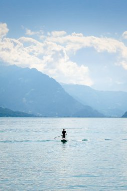 İsviçre 'de Brienz Gölü' nde kürek tahtasında duran bir adamın silueti. Arka planda dağlar. Aktif yaşam tarzı, spor. İnanılmaz bir geçmiş, yaşam tarzı konsepti.