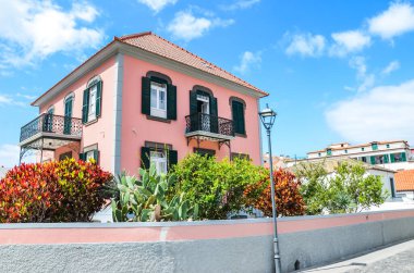 Ribeira Brava, Madeira, Portekiz - 9 Eylül 2019: Madeiran şehrinde geleneksel evleri olan sokak. Pembe yüzlü bir bina ve renkli çiçekler ve çalılarla dolu güzel bir bahçe. Güneşli bir gün