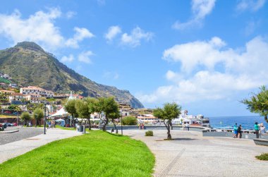 Porto Moniz, Madeira, Portekiz - 13 Şubat 2019: Portekiz yaz tatili beldesinde çimen ve yeşil ağaçlarla gezinti. Arka planda kayalar ve binalar var. Atlantik Okyanusu Kıyısı