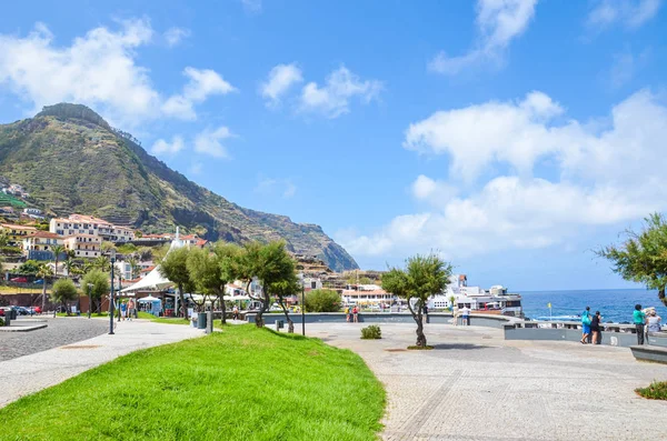 Porto Moniz, Madeira, Portugália - 2019. szeptember 13.: Sétány fűvel és zöld fákkal a portugál üdülőhelyen. Kövek és épületek a háttérben. Az Atlanti-óceán partja — Stock Fotó