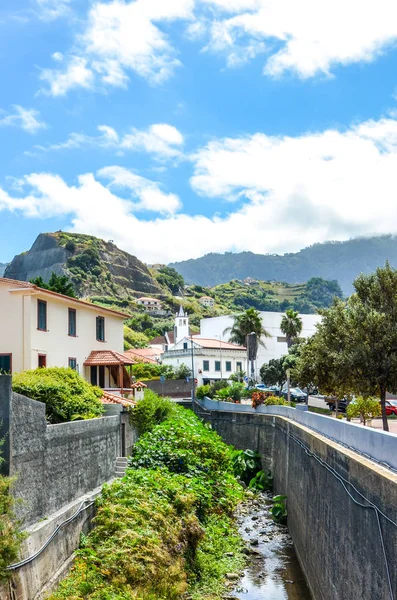 Porto da Cruz, Madeira, Portugal - 24 de setembro de 2019: pitoresca aldeia portuguesa rodeada de montanhas e vegetação verde. Pedras atrás das casas. Fluxo de rio ao longo da rua — Fotografia de Stock