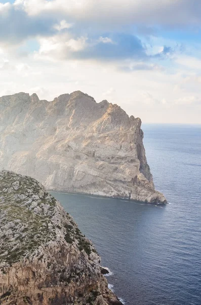 View of the cliffs from Mirador Es Colomer in Cap de Formentor, Mallorca, Spain. Rocks in the Mediterranean surrounded by sea. Sunrays shining on the cliffs. Clouds in the sky. Vertical photo — 스톡 사진