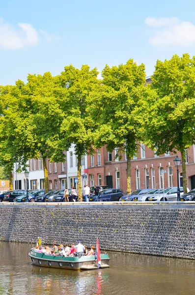 Hertogenbosch, Brabant-Septentrional, Pays-Bas - 9 juin 2018 : Canal d'eau avec bateau touristique dans le centre historique de la ville néerlandaise. Canal entouré d'arbres, de bâtiments et de voitures garées. Photo verticale — Photo